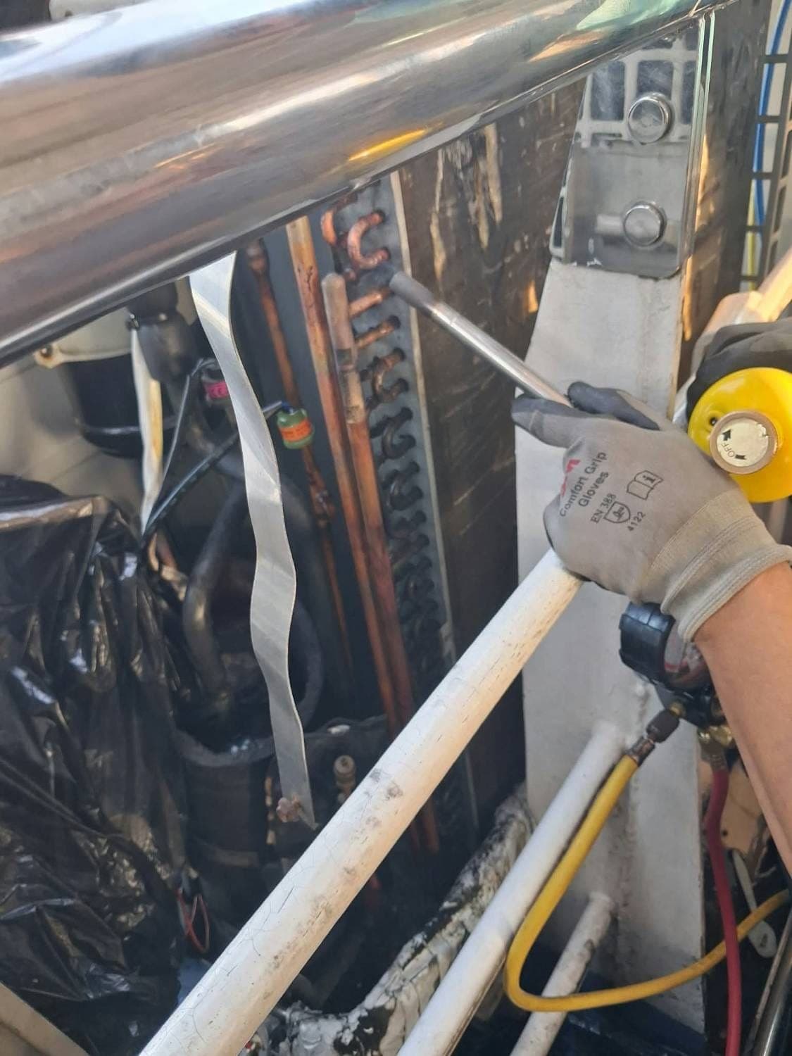 A technician in work gloves checking an aircon's copper refrigerant lines, with gauge hoses attached